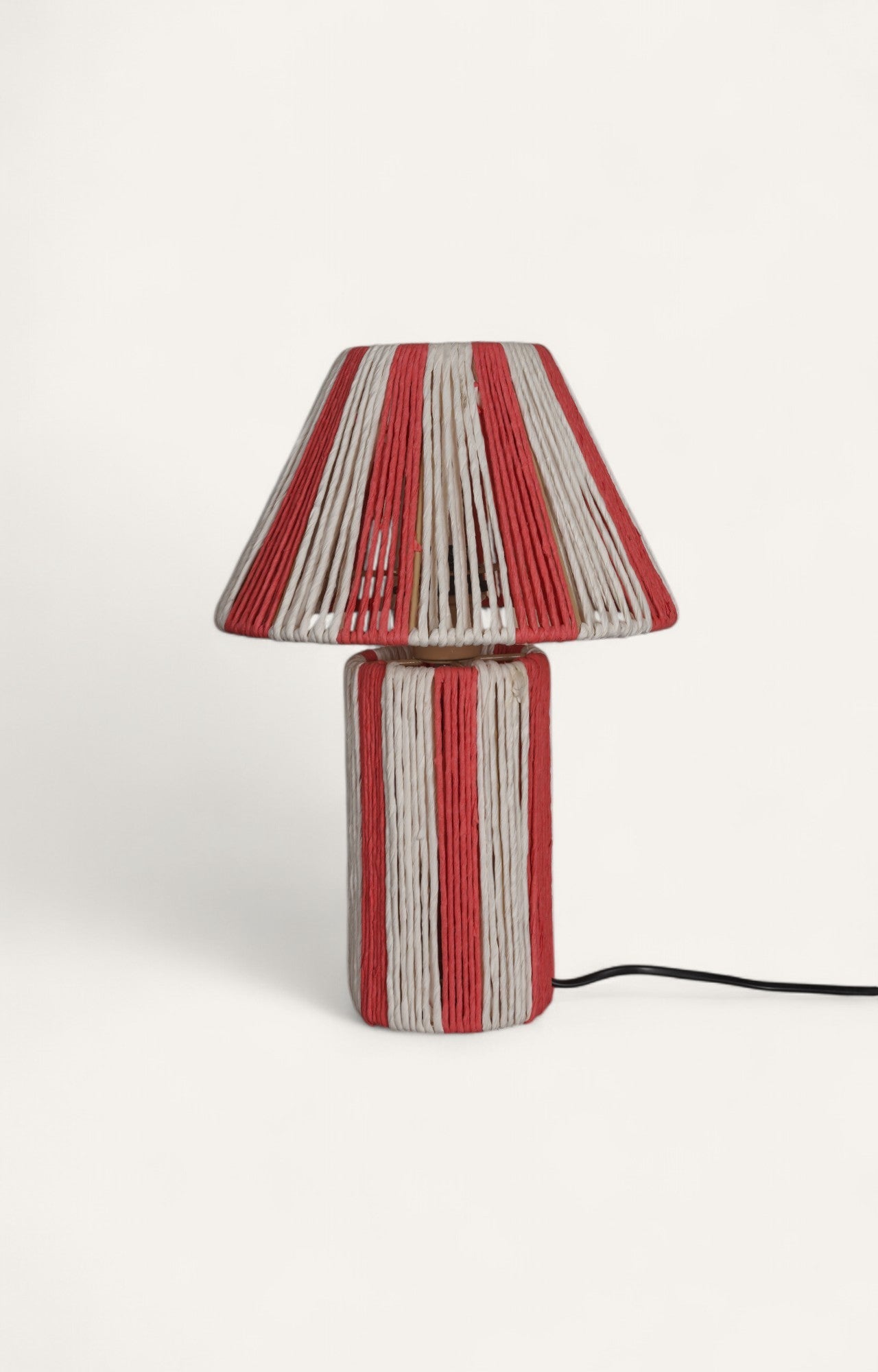 Table lamp with bold red and off-white stripes created from textured raffia ropes around a metal frame.